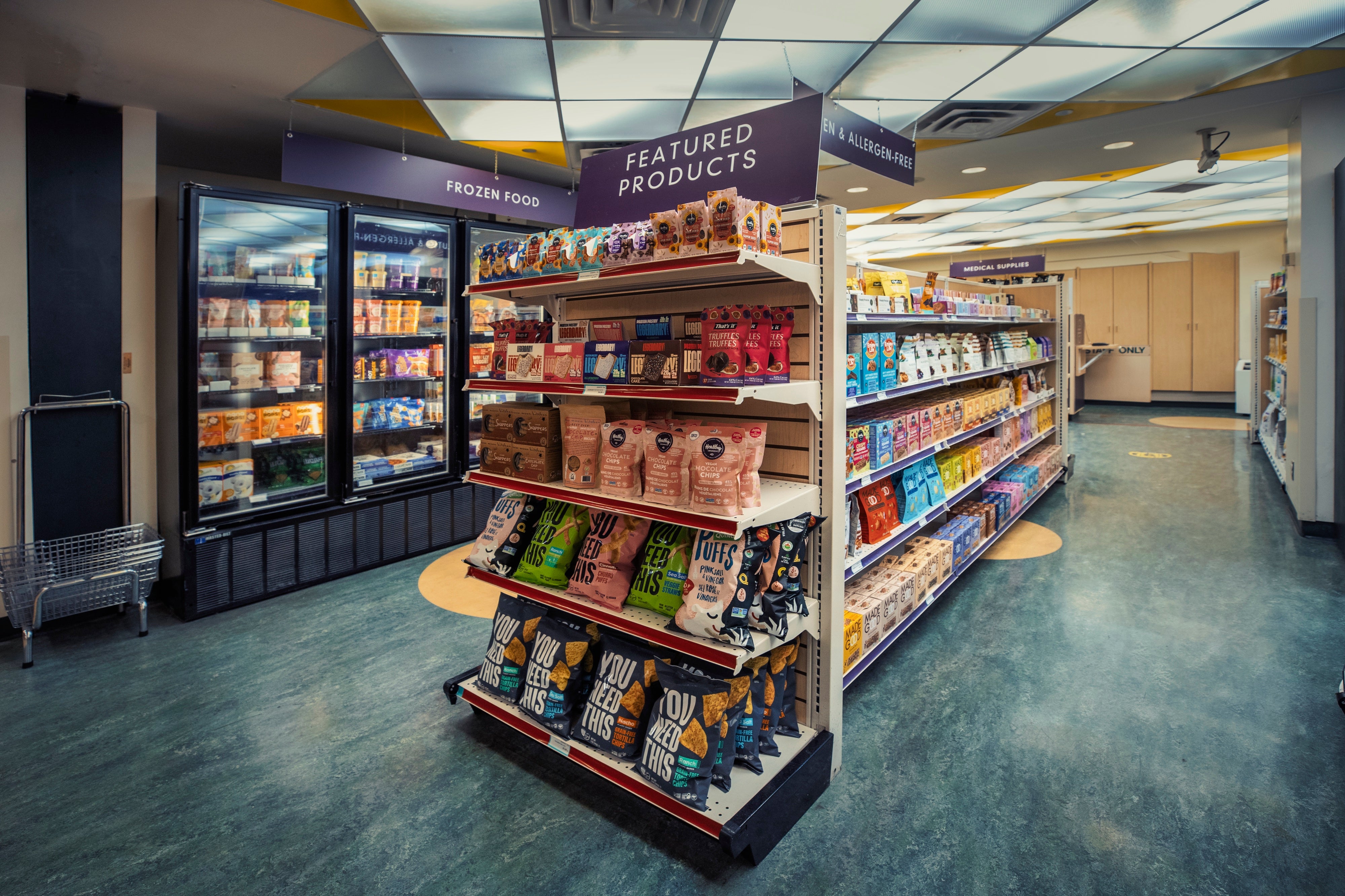 Shelves stocked with packaged foods inside Specialty Food Shop with a purple sign that reads “Featured products.”