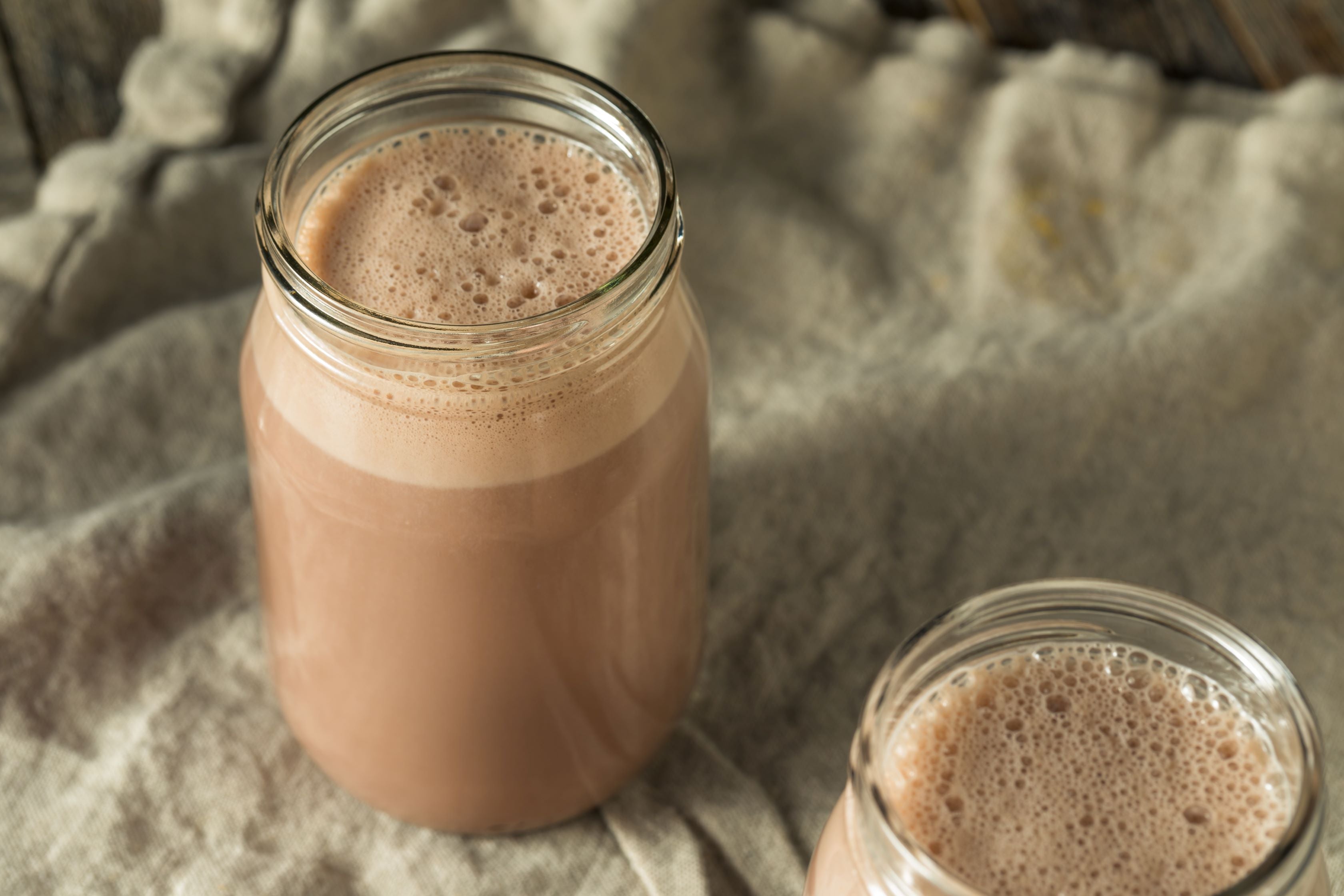 Glass jars filled with a chocolate milkshake in front of a neutral background.